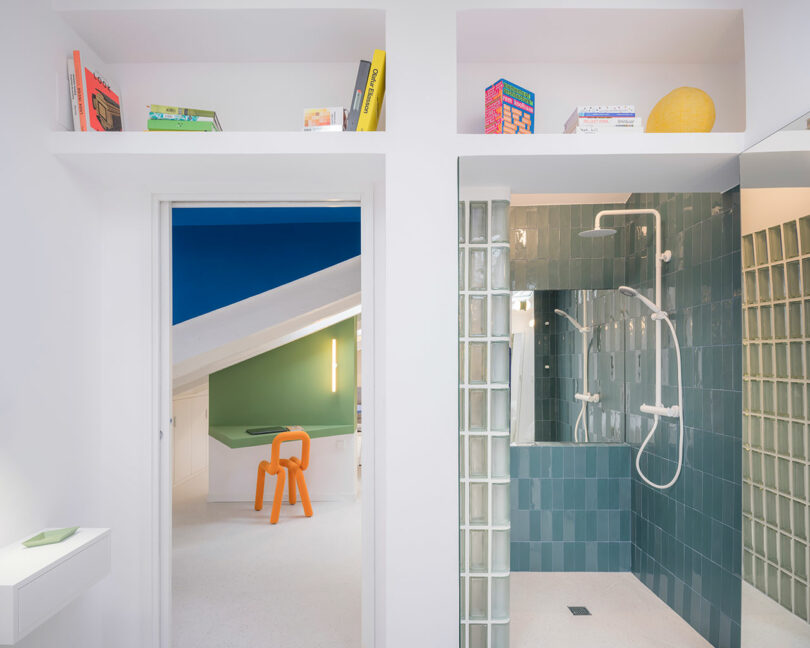 Modern bathroom with adjacent colorful room, showcasing clean lines, tiled shower space, and built-in wall shelves with decorative items.