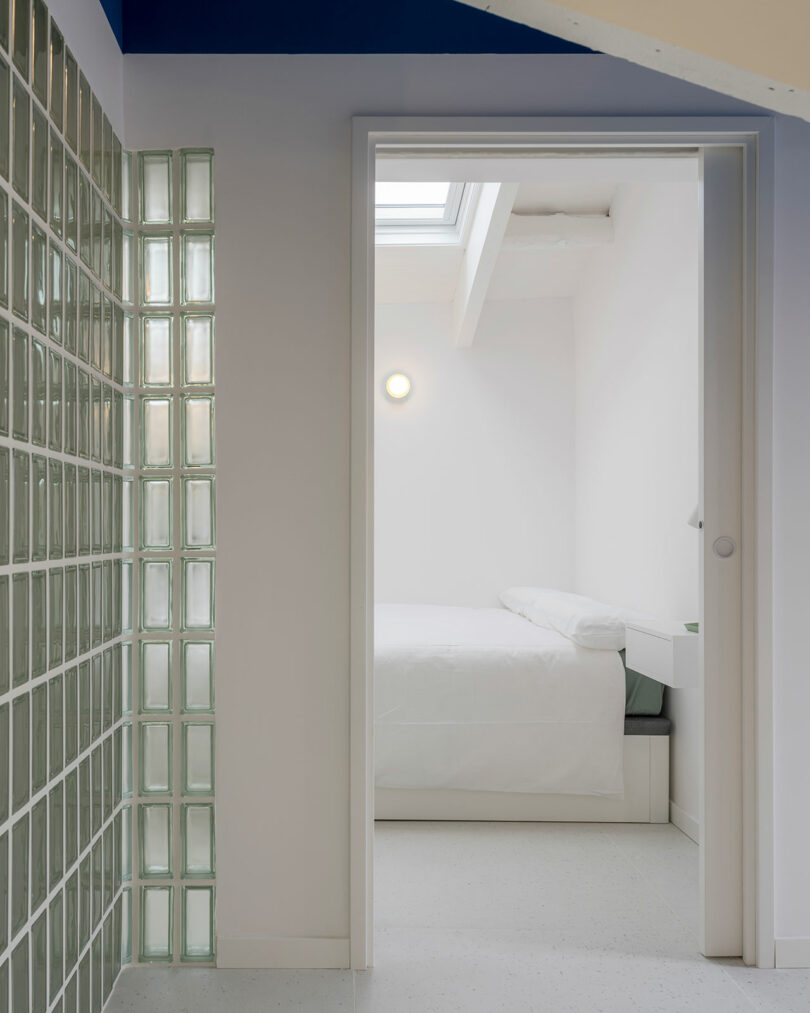 Hallway view with wall of glass bricks looking into minimalist white bedroom