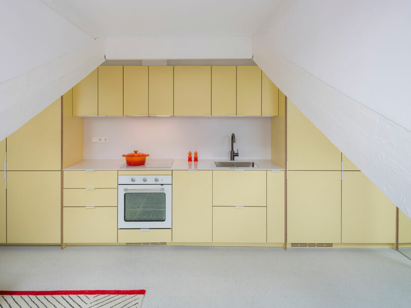 Modern kitchen with yellow cabinetry and a slanted white ceiling.