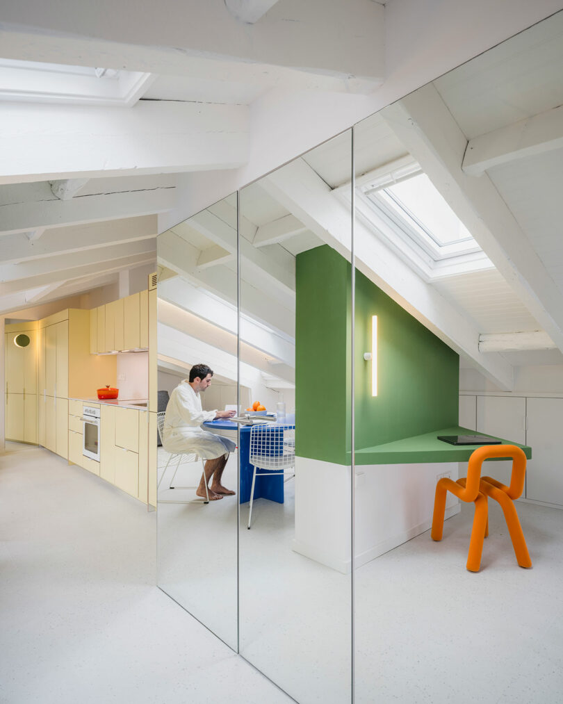 A person working at a desk in a brightly lit, modern attic space with reflective surfaces and colorful furniture.