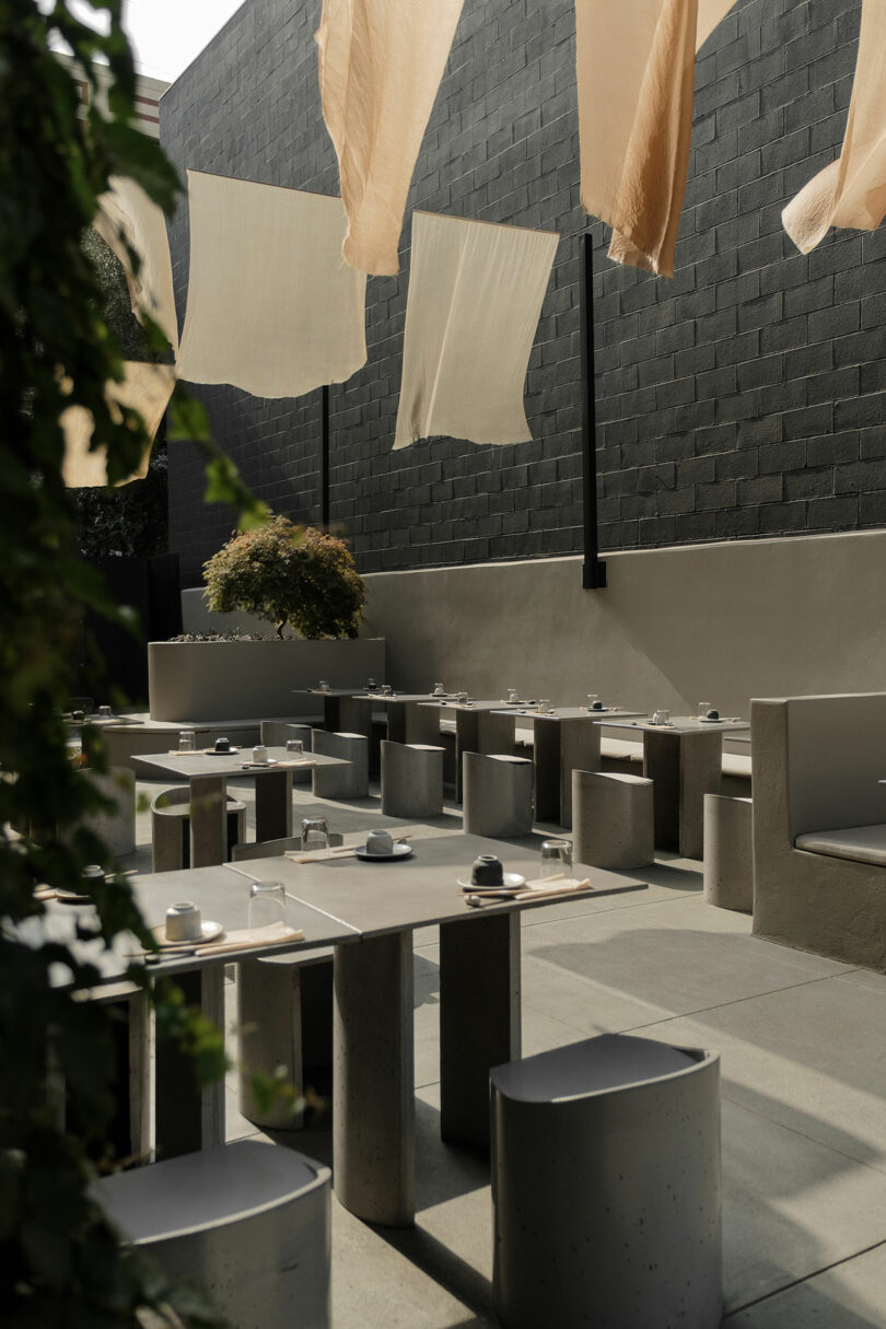 Outdoor dining area with modern concrete furniture and hanging fabric shades.