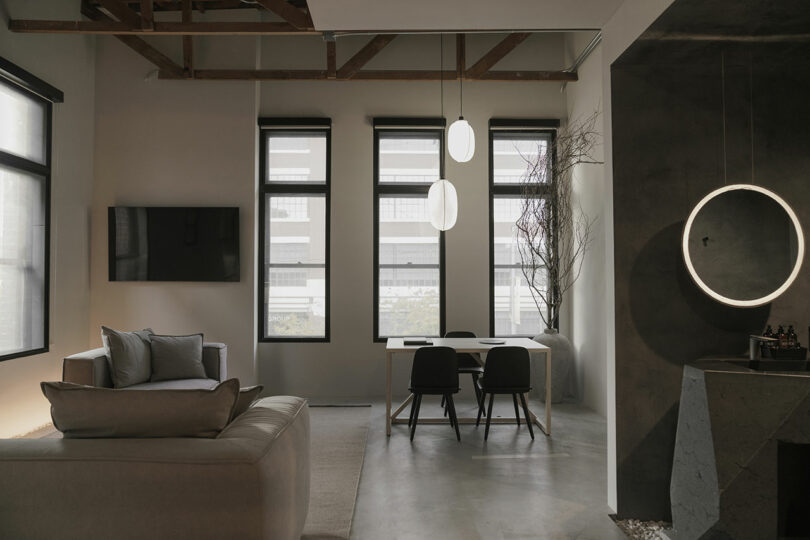 Modern living room with industrial design elements, featuring a sofa, dining area, and circular wall light.