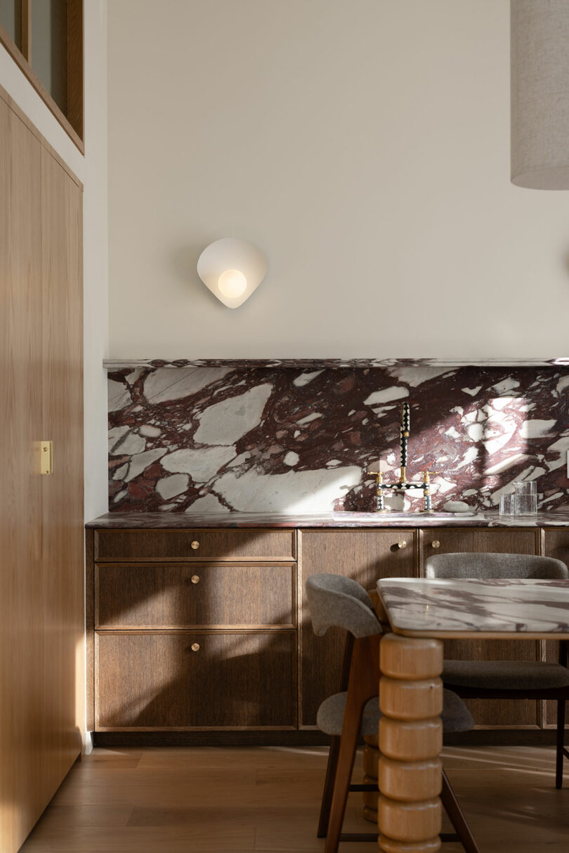 Modern kitchen interior featuring wooden cabinetry and a marble backsplash, with a simple dining area to the side.