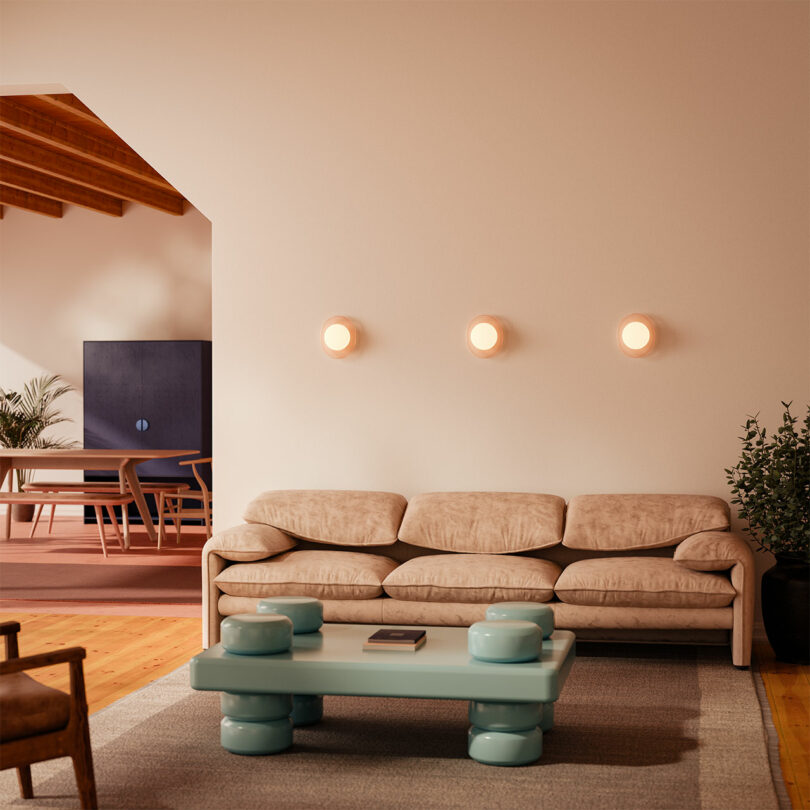 Modern living room with a beige sofa, teal coffee table, ambient wall lights, and a dining area visible in the background.