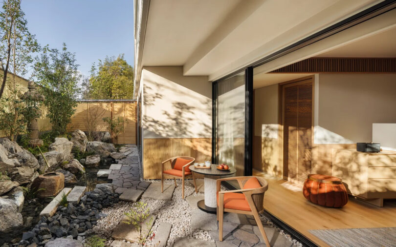 Modern garden guest room deck at the Six Senses Kyoto hotel with sliding glass doors, two chairs, and a table set against a landscaped garden with rocks and a wooden fence.