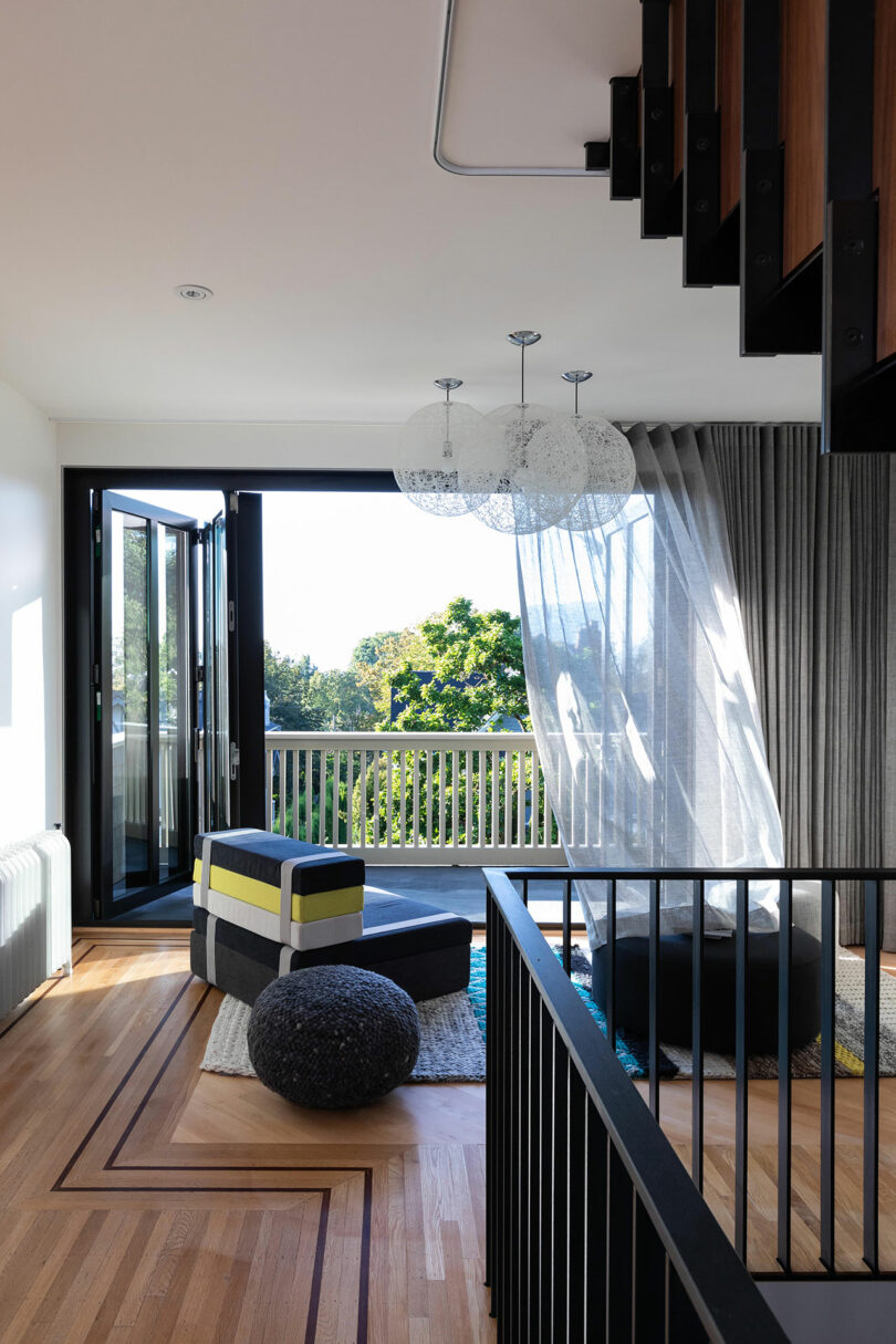 Modern living room with black and yellow chairs, a unique white chandelier, and a balcony view, featuring sleek, and dark wood stair railings.