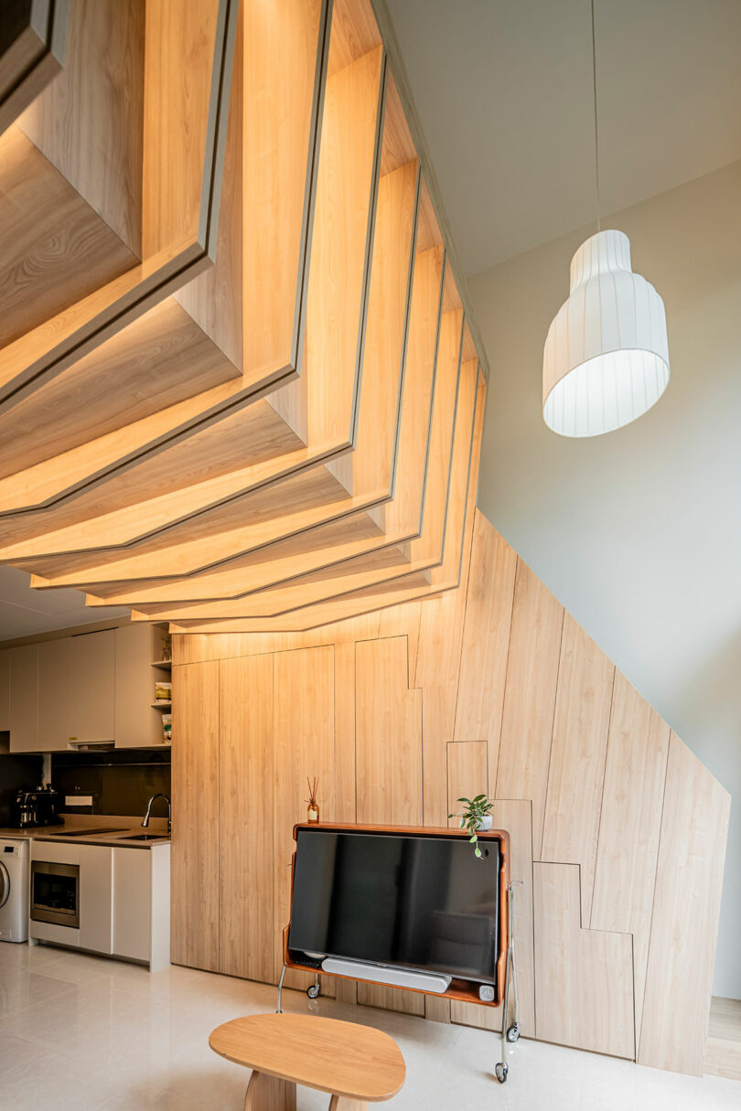 Modern kitchen interior with geometric wooden paneling on walls and ceiling, featuring a vintage tv on a wheeled stand and a hanging pendant light.