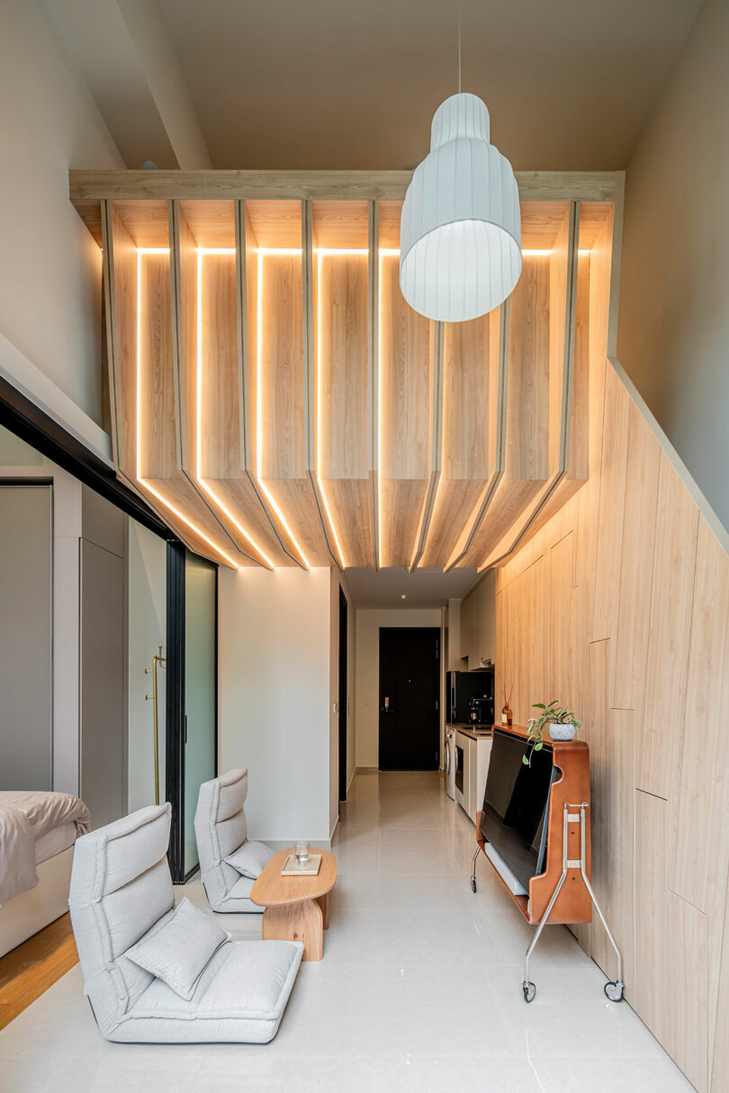 Modern living room with wooden paneled walls and a unique, large ceiling light fixture, featuring cozy chairs and a small table.