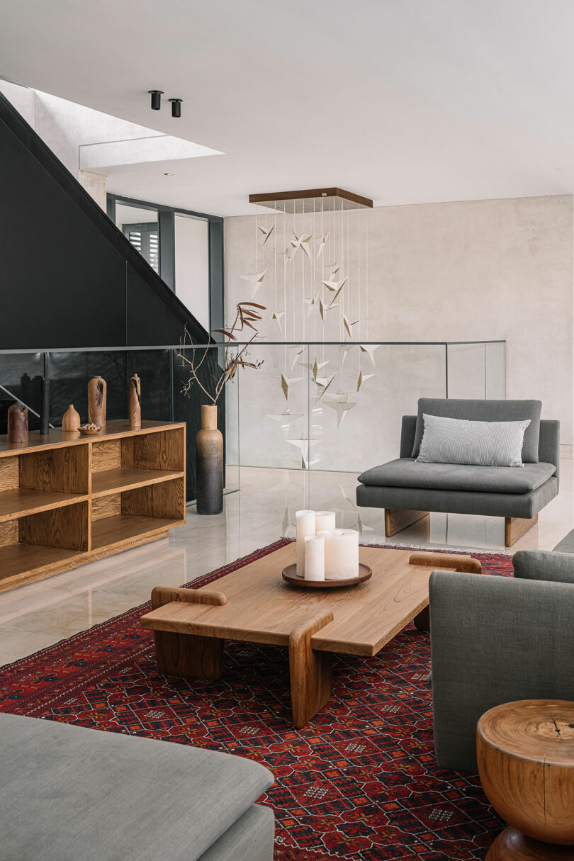 Modern living room with minimalist decor, featuring a gray sofa, wooden furniture, and a red patterned rug. a sculptural mobile hangs above.