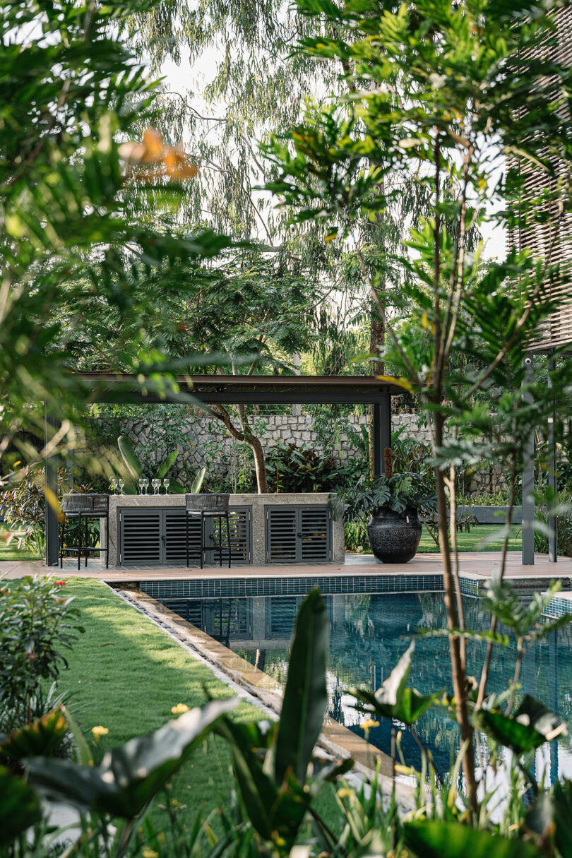 Lush garden with a pool, framed by trees and plants, featuring a modern seating area under a wooden pergola.