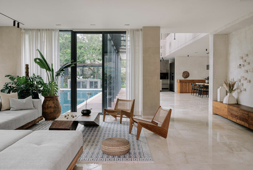 Modern living room with white sofas, wooden chairs, and large windows overlooking a lush garden. neutral tones and minimalistic decor dominate the space.